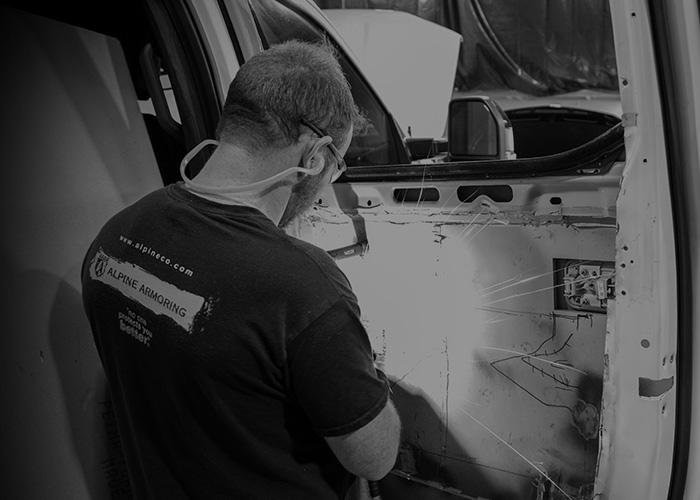 An Alpine Armoring employee working on the interior of a vehicle door while wearing safety goggles and a mask.