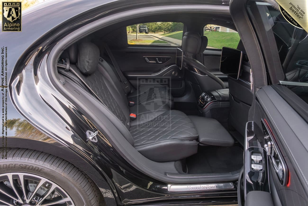 Interior of an armored black Mercedes-Benz S580 sedan showing a leather stitched dashboard, a center console with electronic controls, a large infotainment screen, and intricate leather seating.