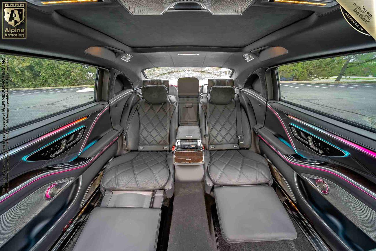 Interior of an armored Mercedes-Benz S 580 Maybach luxury sedan featuring quilted leather seats, ambient lighting, and a central control console. The seats are arranged to face each other with ample legroom and sleek modern design elements.