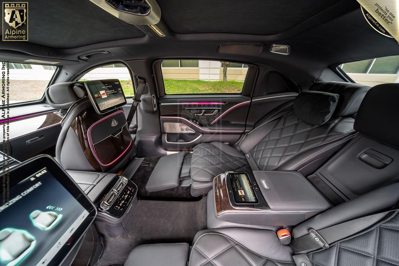 The interior of an armored Mercedes-Benz S 580 Maybach sedan featuring black leather quilted seats, multiple digital screens, and plush amenities.