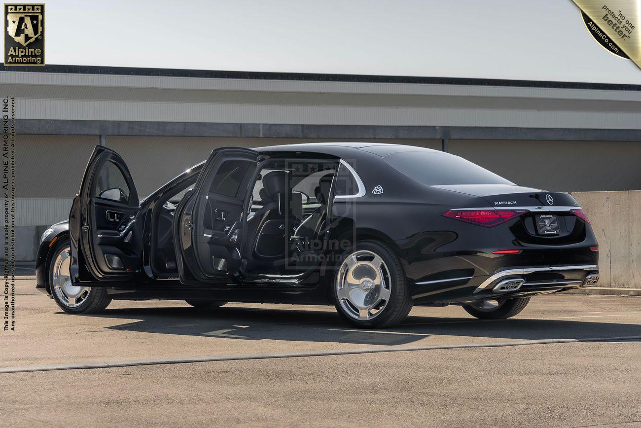 A black bulletrproof Mercedes-Benz S 580 Maybach sedan with both rear passenger doors open, showcasing a spacious and premium interior, parked in an outdoor setting.