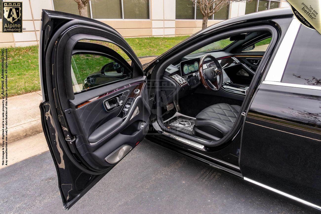 An armored Mercedes-Benz S 580 Maybach sedan with its front passenger door open, showcasing a quilted leather seat and a modern dashboard with digital displays.