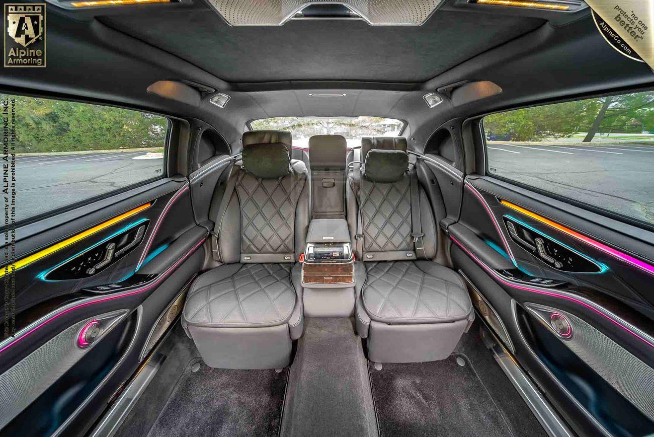 Interior of an armored Mercedes-Benz S 580 Maybach sedan featuring gray quilted leather seats, ambient lighting, and a control panel in the center console, with branding from Alpine Amizonia visible.