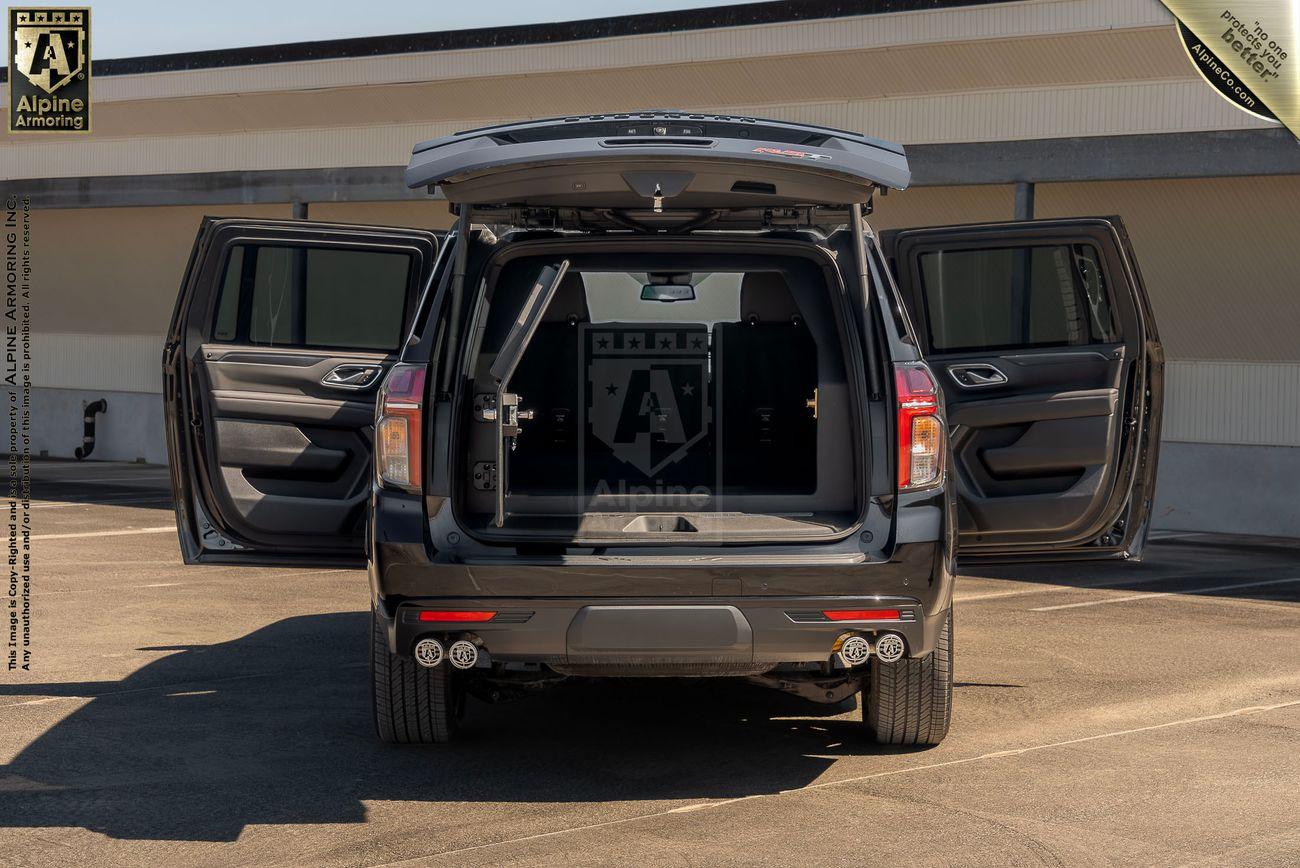 Open rear and side doors of a black armored Chevrolet Suburban LT SUV parked in a lot with visible interior logos from Alpine Armoring.