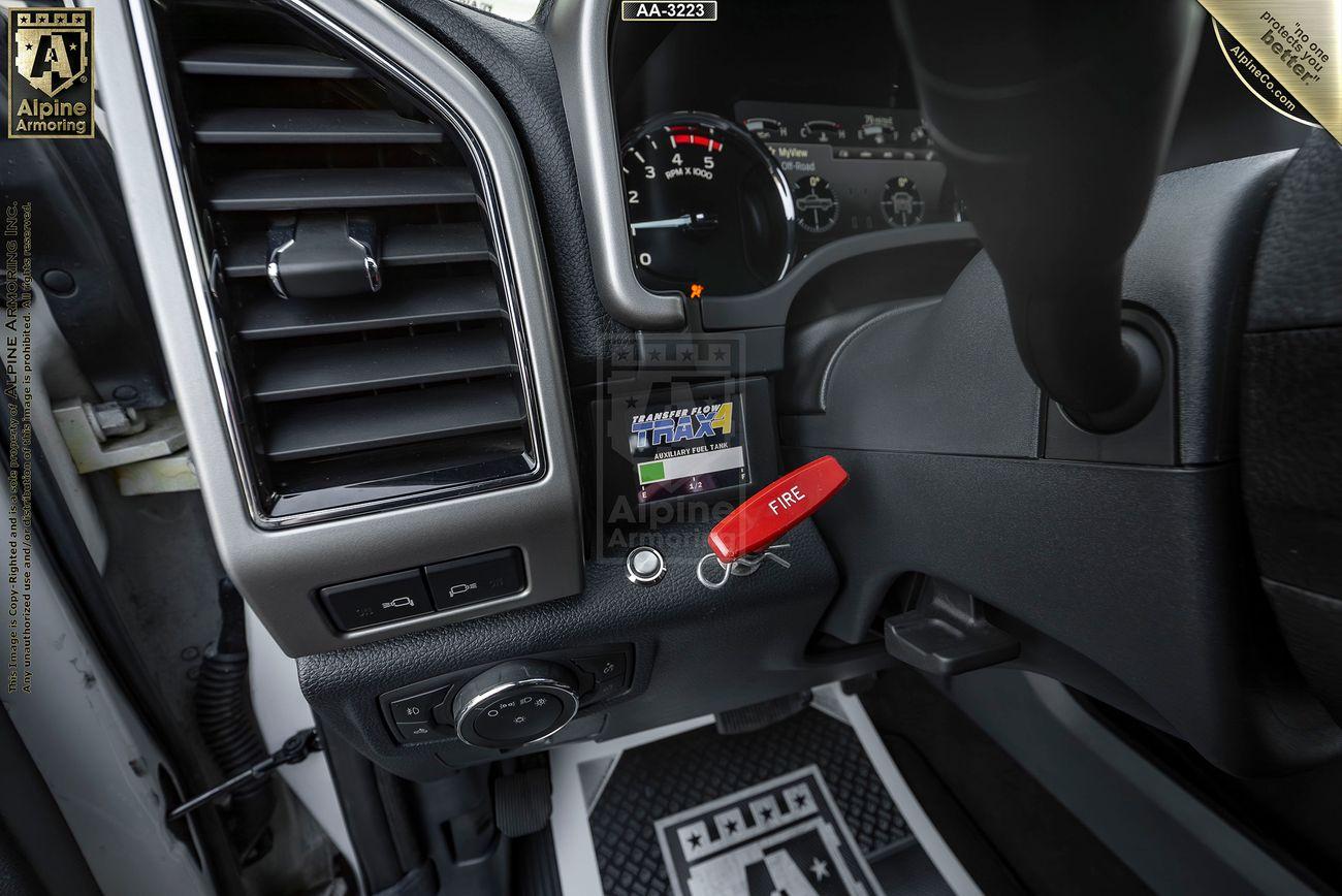 Close-up view of a Mastiff dashboard showing gauges, a "FIRE" safety key tag, and a small digital screen displaying "Arm / Brake Packs" message. Air vent and ignition button also visible.