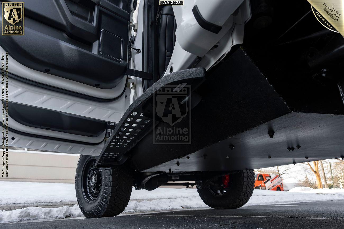 Open armored Mastiff door showing Alpine Armoring shield, heavy-duty steps, and snow-covered street in the background.