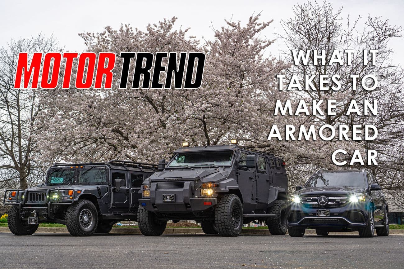 Three Alpine Armoring vehicles are parked in front of blossoming trees. The image includes the "Motor Trend" logo and the text "What It Takes to Make an Armored Car." The vehicles include a Humvee, a heavily modified tactical vehicle, and a Mercedes-Benz.