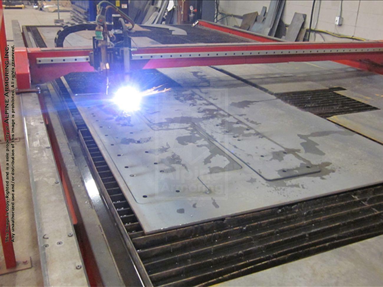 A CNC machine is cutting a sheet of metal with a bright plasma torch. Red rails and a gridded metal bed are visible in the workspace.