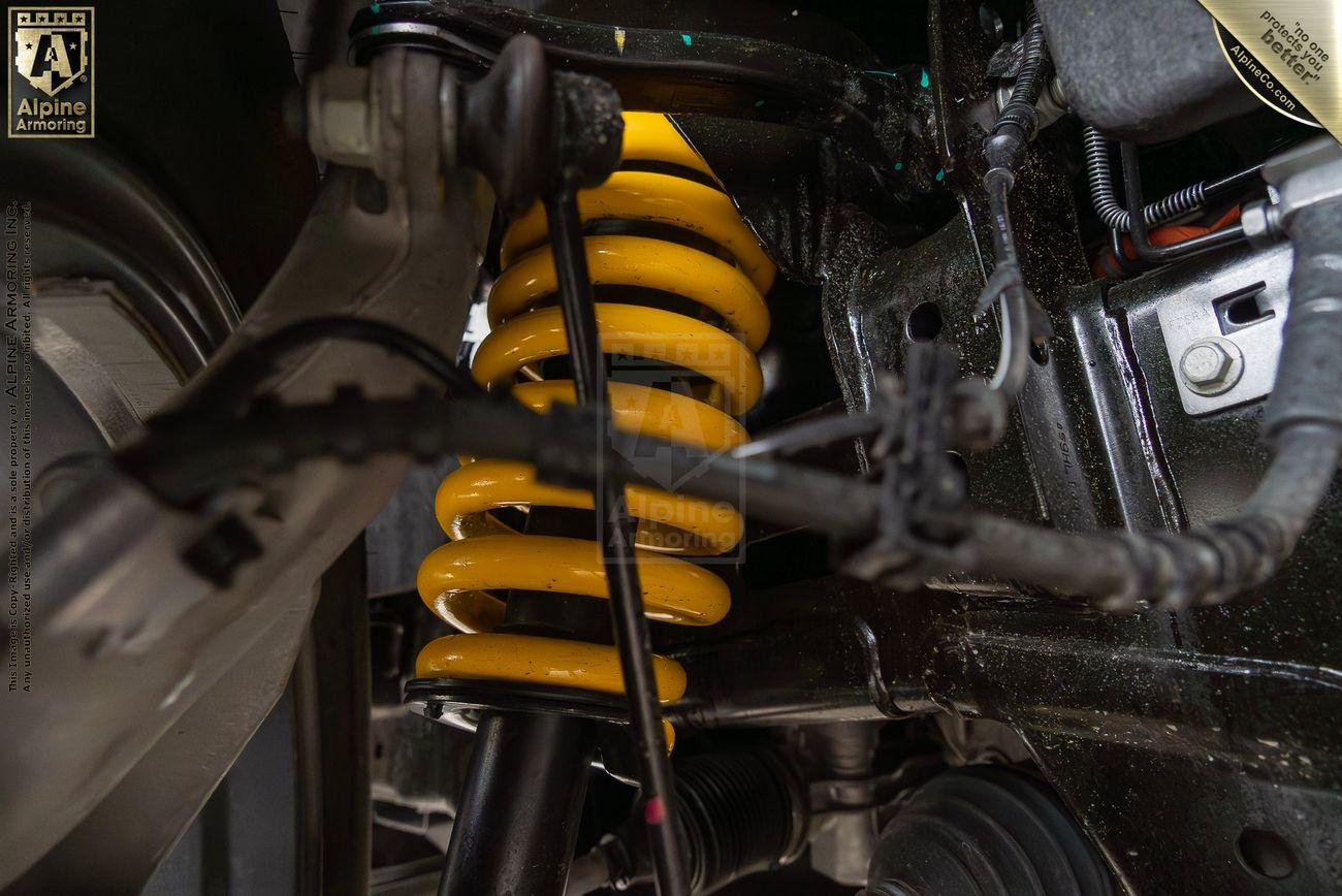 A close-up view of an Alpine Armoring vehicle's yellow suspension coil and associated components, showcasing advanced vehicle dynamics.