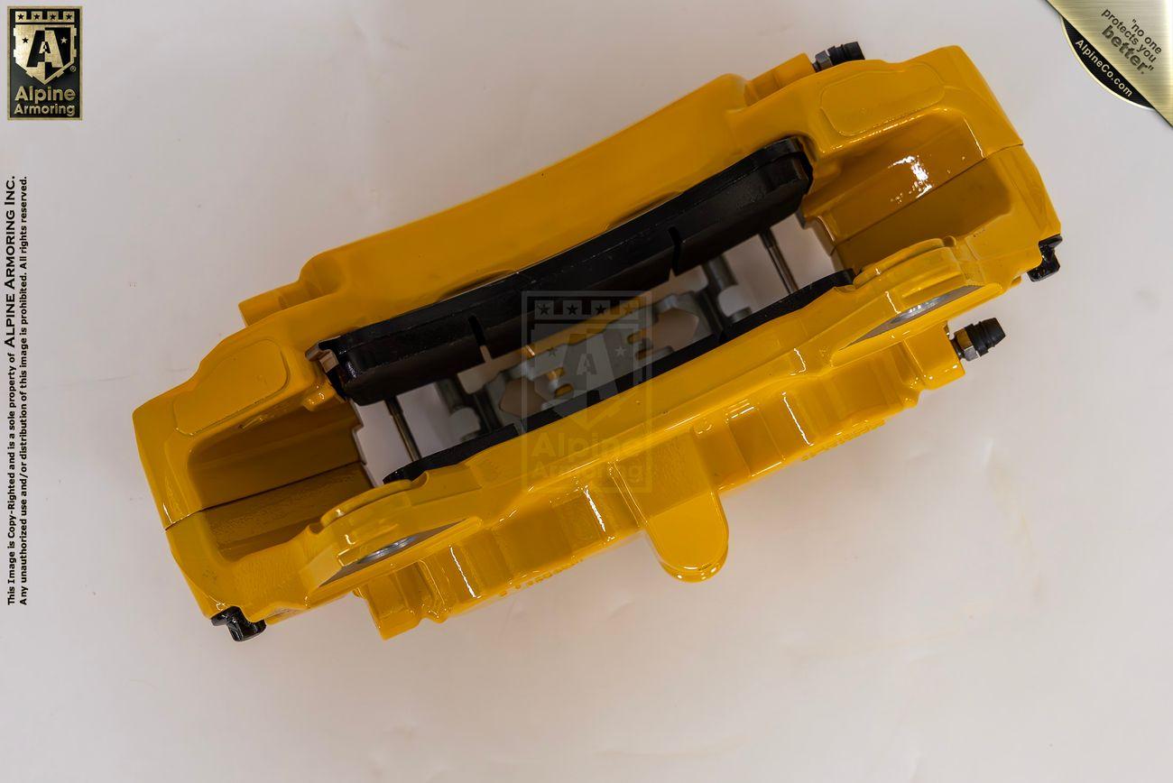 A yellow brake caliper from Alpine Armoring, shown from above, highlighting its robust construction and advanced engineering for armored vehicles.