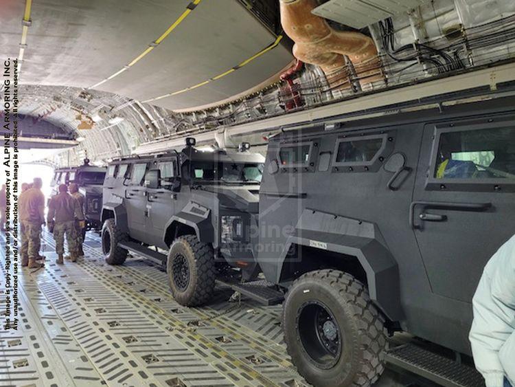 A military transport aircraft's cargo hold with two armored Pit-Bull trucks inside and several personnel standing alongside.