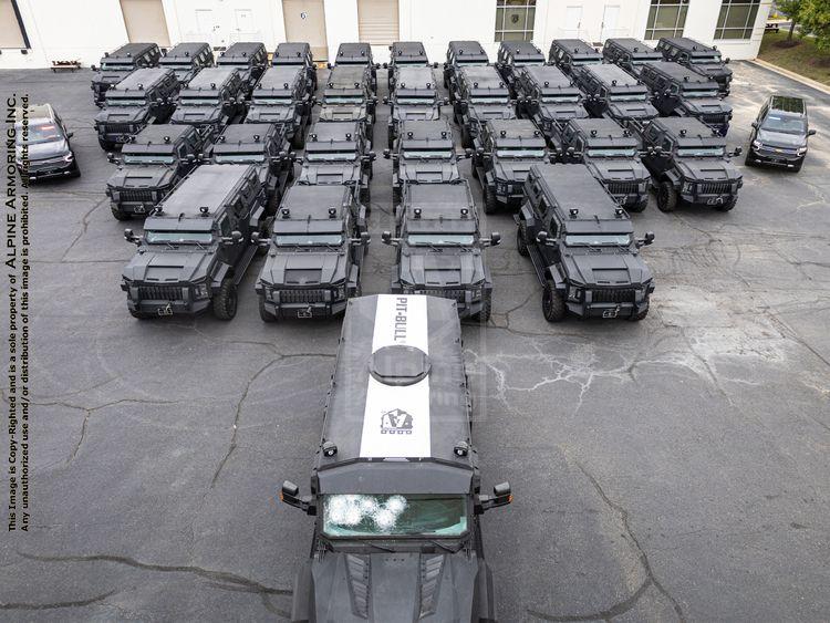 A fleet of black armored Pit-Bulls is parked in an organized formation on a paved surface near a building.