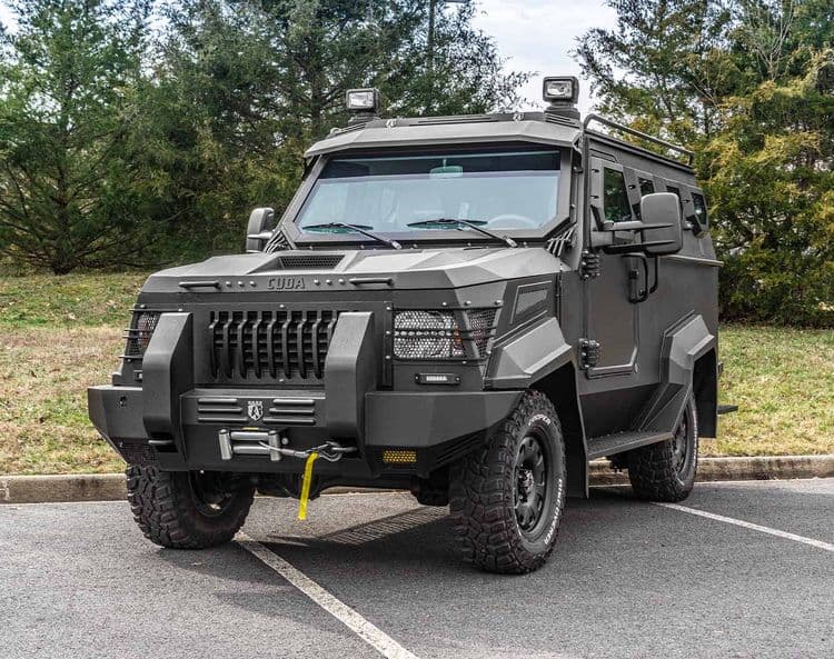 A heavily armored SWAT APC CUDA with off-road tires parked on an asphalt surface, with trees in the background.