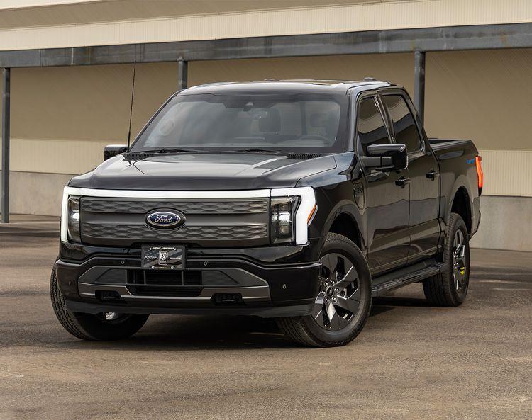 A black Ford Lightning pickup truck is parked on pavement in front of a beige building with a metal canopy.