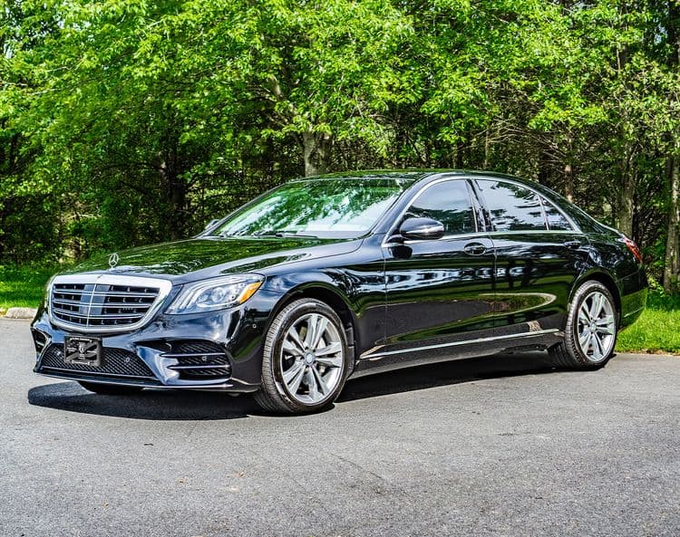 A black armored Mercedes-Benz S560 is parked in an outdoor area on a sunny day.