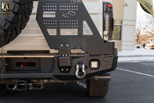 Close-up of the rear bumper and spare tire mount on a Mastiff with a winch, tow hook, and Alpine Armoring branding. Snow is visible in the background.