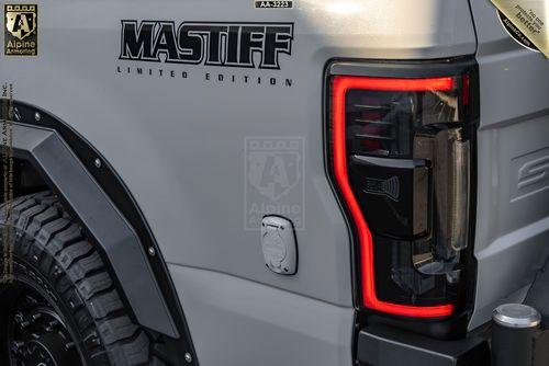 Close-up of the rear side of a white Mastiff displaying the text "MASTIFF LIMITED EDITION", featuring a rugged tire, Alpine Armoring logos, and a taillight with a distinctive red LED outline.